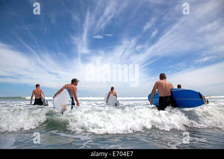 Group of male and female surfer friends wading into sea with surf boards