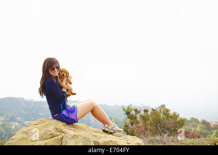 Young woman sitting on rock, holding labrador puppy Stock Photo