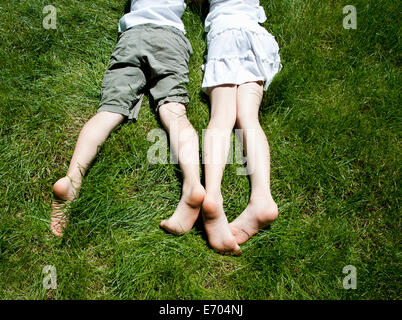 Overhead view of brother and sisters legs as they lay on grass Stock Photo