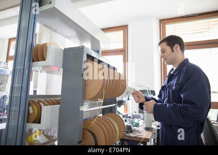 Male electrician pulling power cable from cable drum in workshop