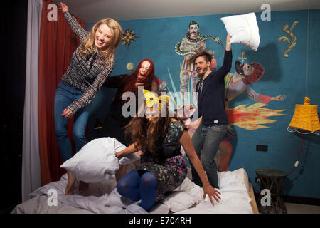 Four adult friends having pillow fight on hotel bed Stock Photo