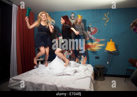 Four adult friends dancing on hotel bed Stock Photo