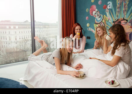 Four young women friends breakfasting on hotel bed Stock Photo