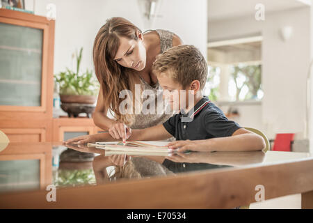 Mother and son looking down at homework at dining room table Stock Photo