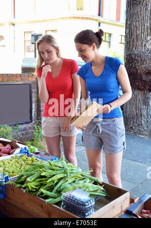 Two young women looking at vegetables at market stall Stock Photo