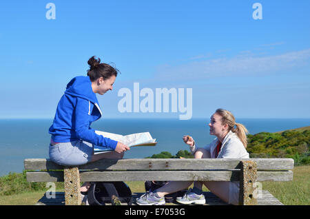 Two young women sitting on bench with map Stock Photo