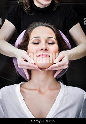 Female masseur massaging young woman's chin in beauty salon Stock Photo
