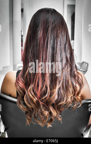 Rear view of young woman in hair salon with long brunette hair with waves and pink highlights Stock Photo