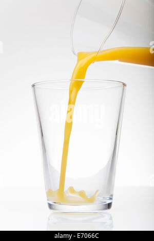 Fresh orange juice pouring from jug into drinking glass Stock Photo