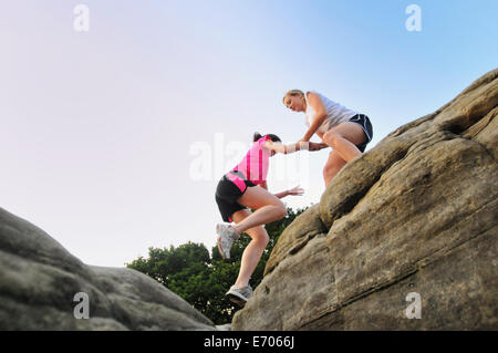 Two young women runners helping each other on top of rock formation