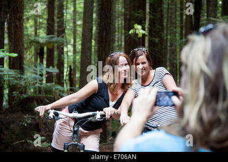 Over shoulder view of women mountain bikers posing for photograph on smartphone in forest Stock Photo