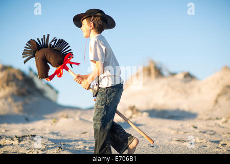 Boy with hobby horse dressed as cowboy in sand dunes Stock Photo