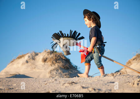 Boy dressed as cowboy with hobby horse in sand dunes Stock Photo