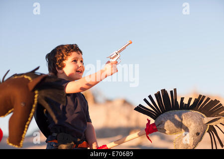 Boy dressed as cowboy with hobby horse and toy gun in sand dunes Stock Photo