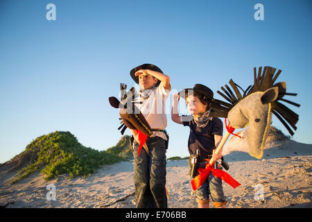 Two brothers dressed as cowboys shading eyes with hands Stock Photo