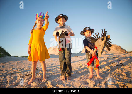Sister and brothers dressed as native american and cowboys pointing from sand dunes Stock Photo