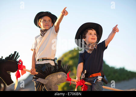Two brothers dressed as cowboys pointing from sand dunes Stock Photo