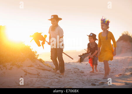 Three children dressed as native american and cowboys in sand dunes Stock Photo