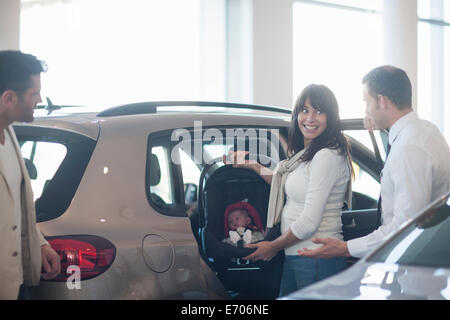 Mid adult couple with baby girl trying out baby seat in car dealership Stock Photo