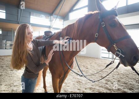 Female horseback rider grooming horse in indoor paddock