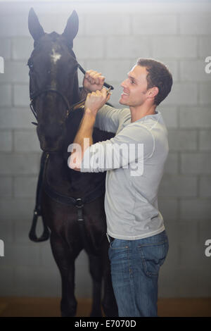 Male stablehand putting bridle onto horse in stables Stock Photo