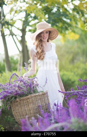 Portrait of beautiful young woman in meadow carrying basket of purple flowers