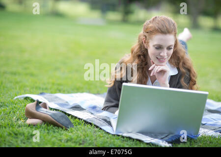Young woman reclining on picnic blanket using laptop in park Stock Photo