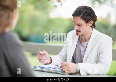 Over the shoulder view of businessman in garden making notes in diary Stock Photo