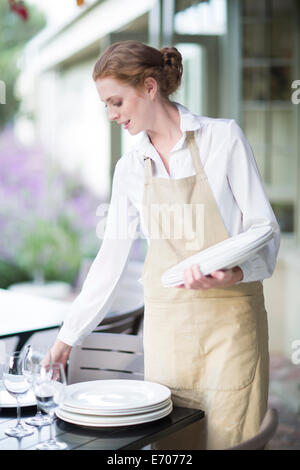 Waitress organizing plates on table in patio restaurant Stock Photo