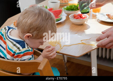 Male toddler accidentallyspilling orange juice at breakfast table Stock Photo