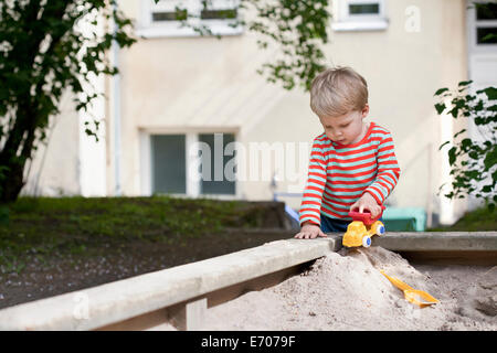 Male toddler pushing toy car in sand pit in garden Stock Photo