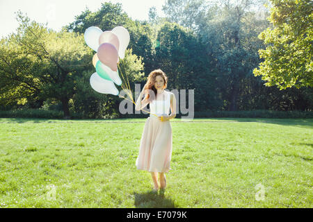 Portrait of shy young woman in park holding a bunch of balloons Stock Photo