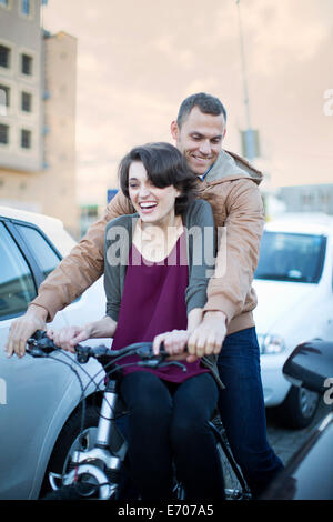 Young woman sitting on bicycle crossbar moving through city traffic jam Stock Photo