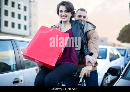 Young woman sitting on bicycle handlebar moving through city traffic jam Stock Photo