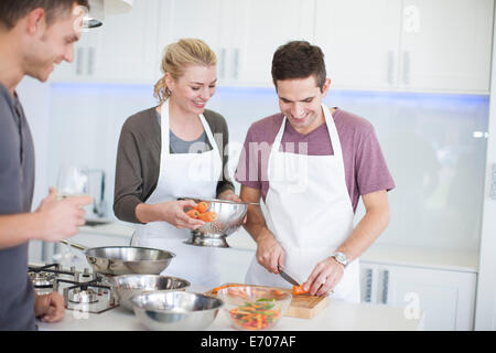 Mid adult man chopping carrots whilst friends watch in kitchen Stock Photo