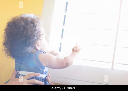 Mother holding baby daughter up to window Stock Photo