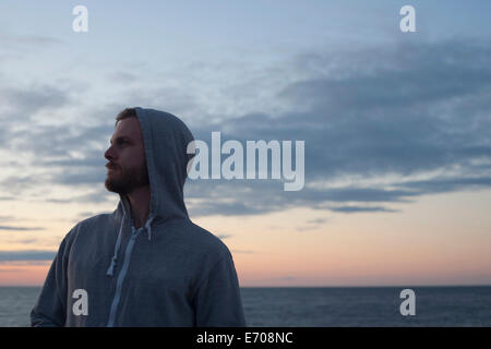 Mid adult man in hooded top gazing over his shoulder at coast, Gloucester, Massachusetts, USA Stock Photo