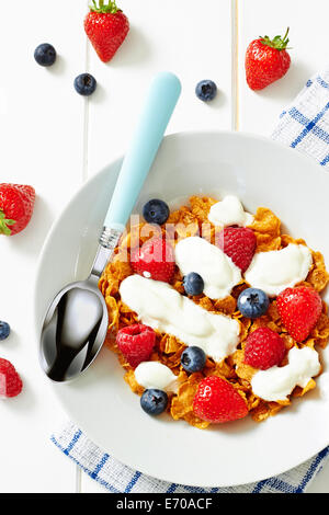 Top view showing breakfast with cornflakes, berries and yogurt on a white wooden table Stock Photo