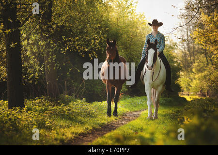 Female western rider on a Paint Horse, Black Tobiano colour pattern, leading a bay Shagya Arabian horse, riding bareback through Stock Photo