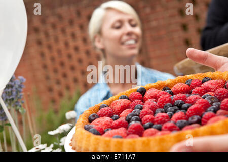 Two female friends with fruit flan at garden party Stock Photo