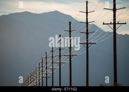 Power lines in rows across the landscape, against a mountain and sunset sky. Stock Photo