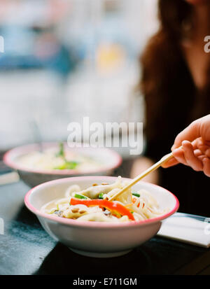 A person's hand holding chopsticks and stirring a dish of noodles. Stock Photo