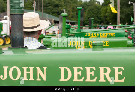 A man in a straw hat sits in a row of John Deere tractors on display at a John Deere tractor expo. Stock Photo