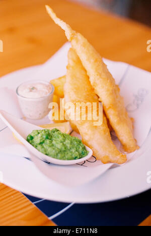 Traditional food, fried battered fish and chips, with mushy peas and tartare sauce on a plate. Stock Photo