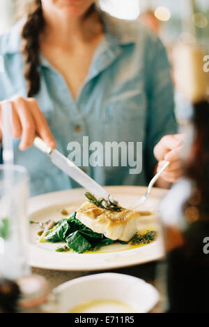 A woman eating a meal, a dish of fish and green vegetables. Stock Photo