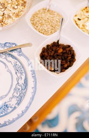 A tabletop with a blue and white plate, bowls of granola, oats and raisins. Stock Photo