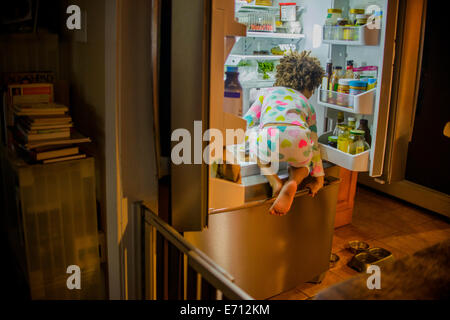 Rear view of girl sneaking food and drink from the refrigerator at night Stock Photo