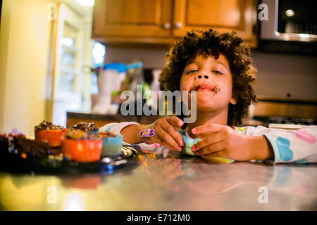 Portrait of girl with chocolate covered mouth eating cupcakes Stock Photo