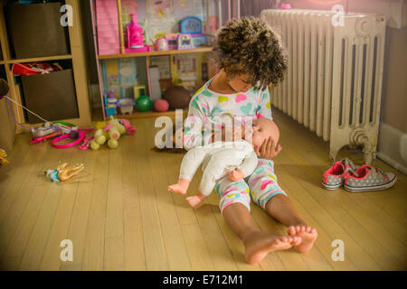Girl sitting on playroom floor feeding doll Stock Photo