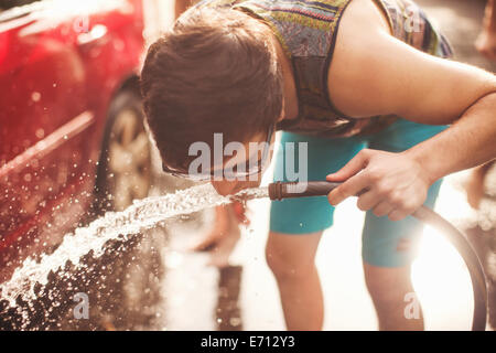 Young man drinking water from hosepipe Stock Photo